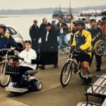 Pam Horton leads a group of people biking/walking on the sea wall. She uses an electric scooter.