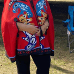 Photo of Louella Vincent. She is standing and smiling, wearing a red jacket that depicts various animals in Indigenous style on the front.